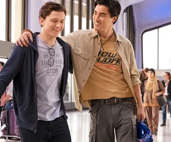 Two young men smiling with arms around each other in an airport scene from "Spider-Man: Far From Home".