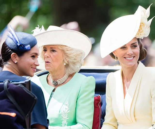 Women in elegant hats seated together during a public outdoor event.