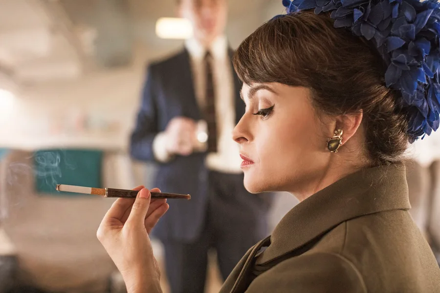 Helena Bonham Carter as Princess Margaret in "The Crown," elegantly smoking with a man in the background.