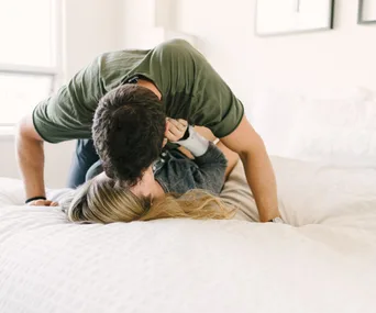 Couple lovingly embracing on a bed in a bright room.
