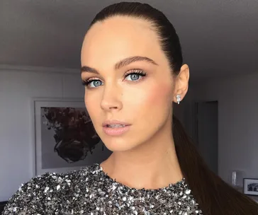 Woman in a sparkly dress with pulled-back hair and earrings, showcasing elegant makeup in a well-lit room.