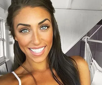 Woman smiling indoors, with long dark hair, wearing a white top, and bright lighting.