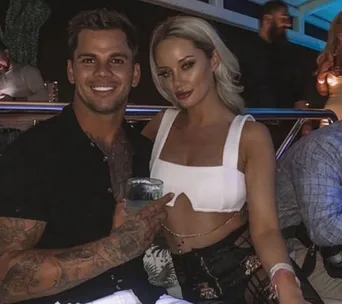 Two people smiling, seated closely at a nighttime event. One holds a drink, the other wears a white top.