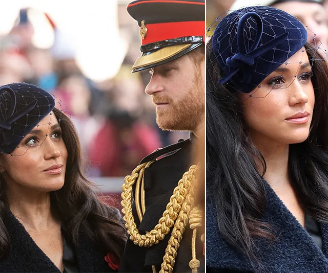 Meghan Markle in a navy blue coat and hat at a public event beside a man in uniform.