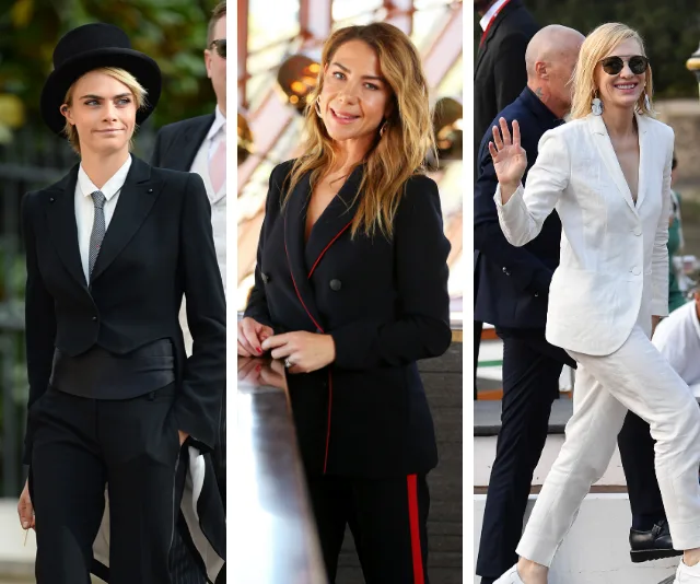 Three women in stylish suits: one in a tuxedo with hat, one in a black suit with red trim, and one in a white suit waving.