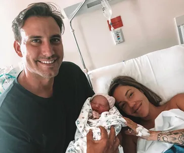 New parents smiling with their newborn baby in a hospital room.