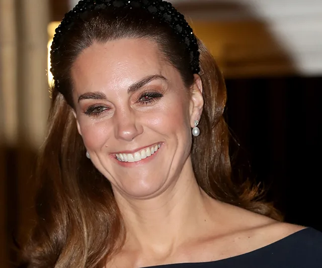 A smiling woman with long hair wearing a black headband and earrings.