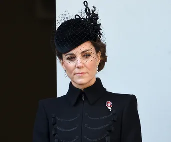 Woman in black outfit with veil and brooch at formal event.