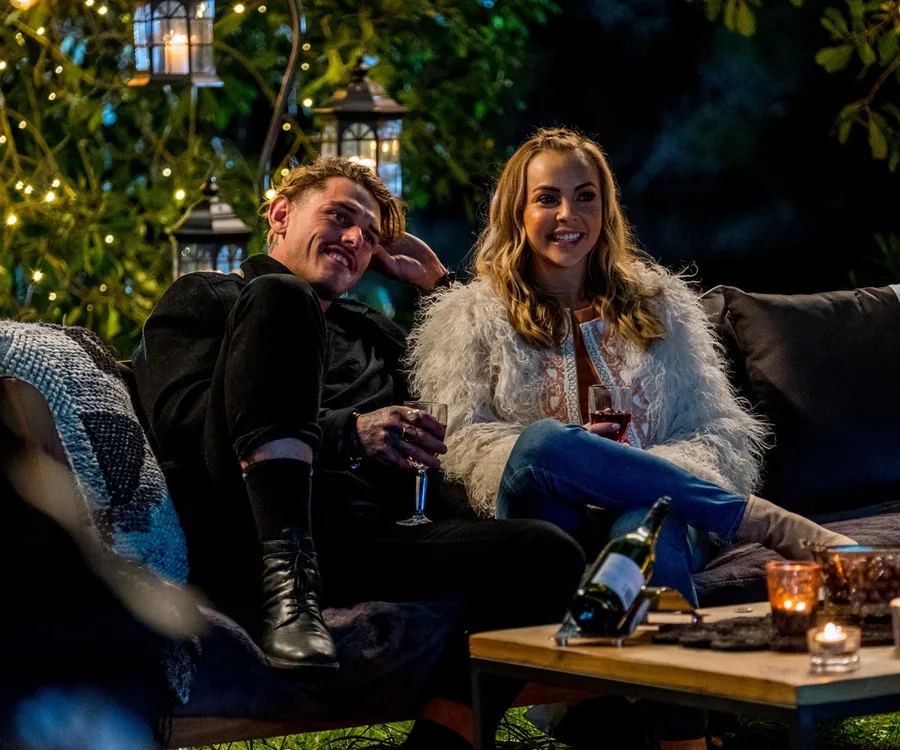 A couple sitting on a sofa outdoors, drinking wine, with fairy lights in the background creating a cozy atmosphere.