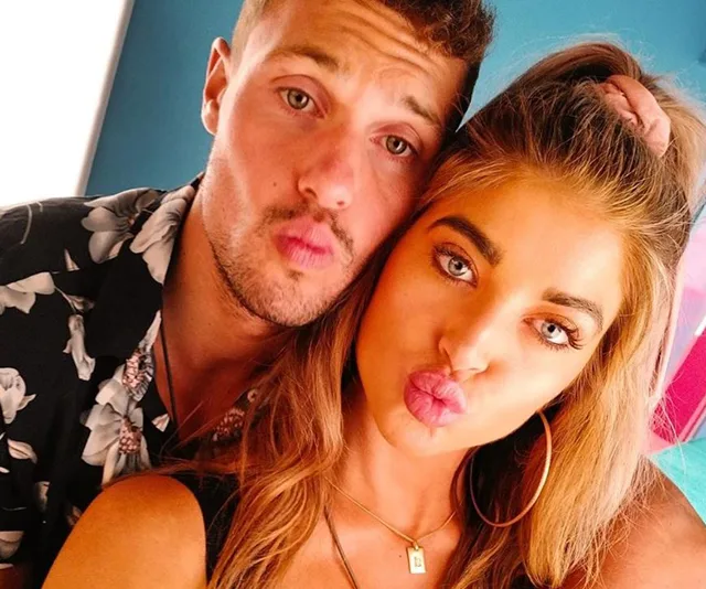 A couple posing for a selfie, making pouty lips, with the man in a floral shirt and the woman wearing hoop earrings.