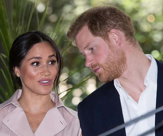 Meghan Markle and Prince Harry at an outdoor event, surrounded by greenery, engaged in conversation.