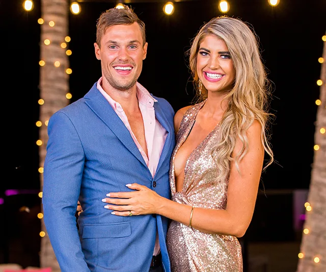 Couple smiling under string lights; woman in a glittery dress, man in a blue suit.