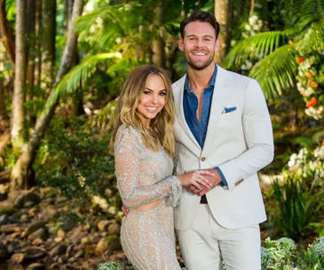 A couple smiling and holding hands in a lush, green garden setting.