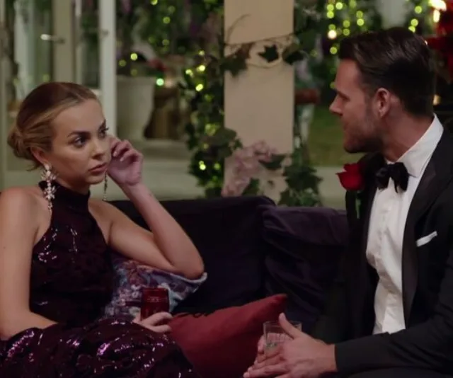 Man in tuxedo and woman in elegant dress sitting on a couch, engaged in conversation at a formal event.