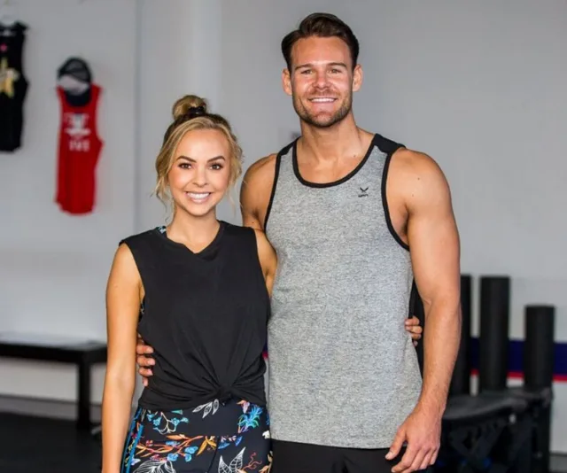 A man and woman smiling and posing in gym clothing inside a workout area.
