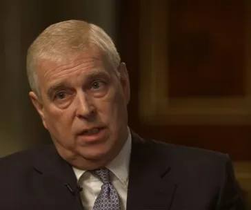 A man in a suit and tie speaking during a formal interview, with a serious expression.