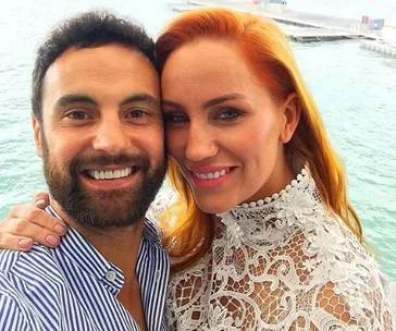 Couple smiling together near the water, with the woman in a lace top and man in a striped shirt.