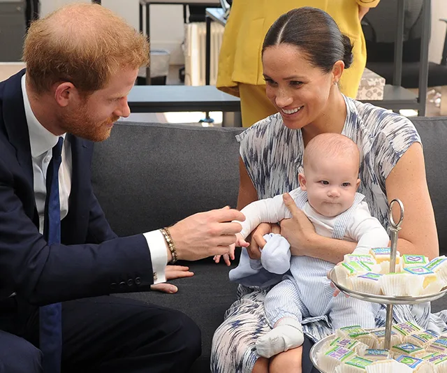 Family sitting on a couch with a baby, smiling, next to a table with small cakes.