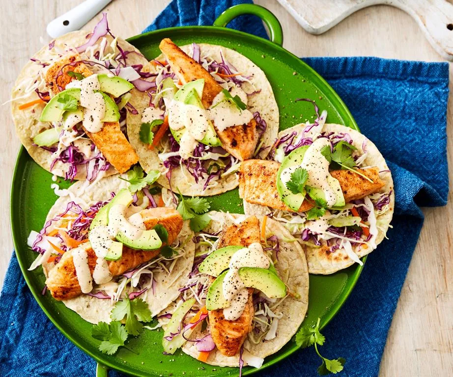 Grilled fish tacos with avocado, cabbage slaw, and drizzle on a green platter.