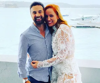 Couple smiling and embracing near a waterfront, dressed in casual and lace attire, with seaplanes in the background.