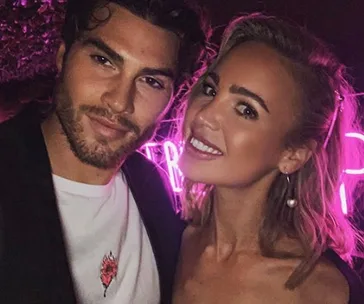 A man and a woman smiling together with neon pink lights in the background.