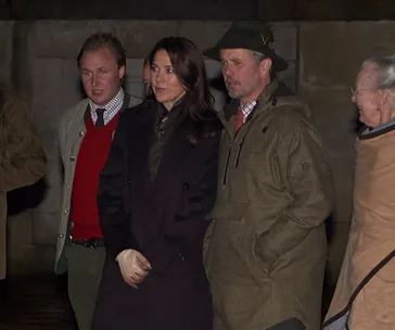 Royal figures attending a deer hunting event, dressed warmly and standing together outdoors.