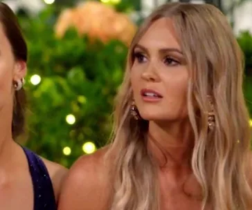 Two women seated; one with long blonde hair is looking to the side, with a blurred garden background.