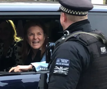 A woman in a car smiles and talks to a police officer standing outside.