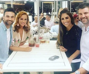 A group of four people sitting at an outdoor cafe table, smiling with drinks on the table.