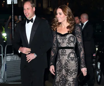 A man and a woman in formal attire attending an event, with onlookers in the background.