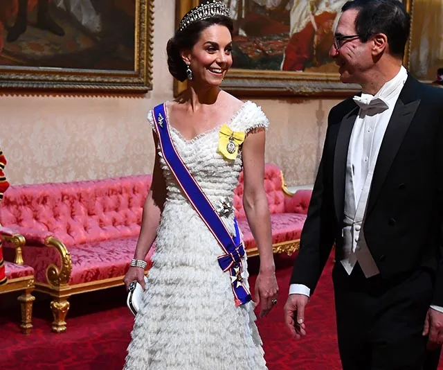 Kate Middleton wearing a tiara and white gown, smiling, with a man in a tuxedo at a formal event.