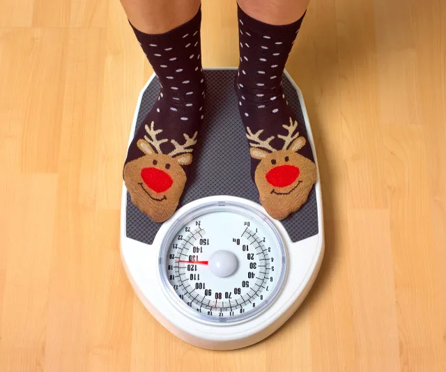 Person wearing reindeer socks standing on a mechanical scale on wooden floor.