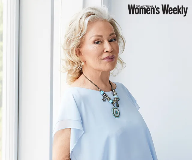 Woman in light blue top with necklace, standing by a window, featured in The Australian Women's Weekly magazine.