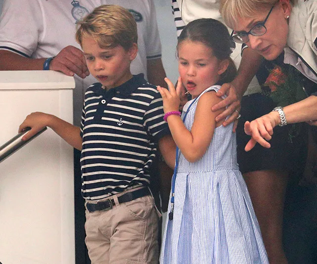 Two young children stand together with an adult, looking down as if observing something below.