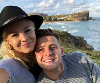 Couple smiling together by the seaside with a scenic view of cliffs and ocean.