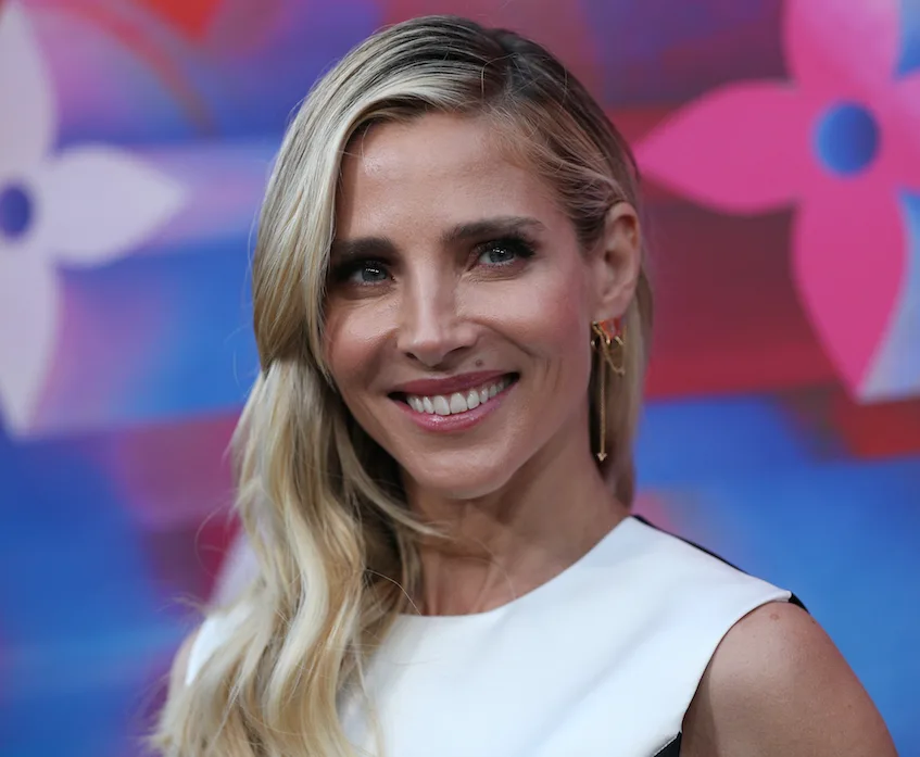 Elsa Pataky smiling at a colorful event backdrop, wearing a white dress.