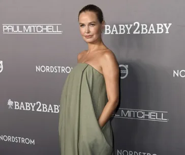 A person poses on the red carpet in a strapless green dress at a Baby2Baby event.
