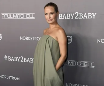 A person poses on the red carpet in a strapless green dress at a Baby2Baby event.