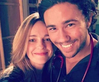 A smiling woman and man with a stethoscope take a selfie together indoors.