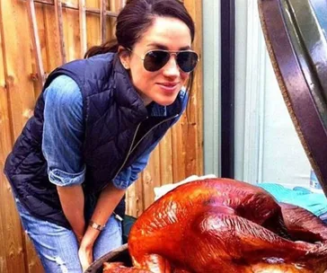 A woman in sunglasses smiles while posing next to a cooked turkey on a grill outdoors.
