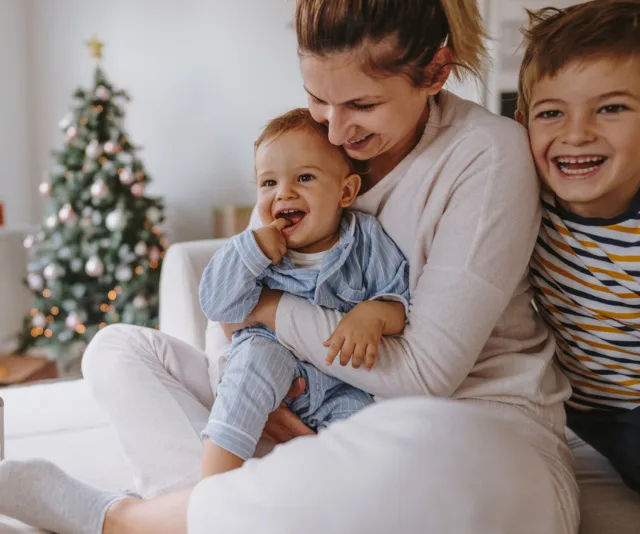 A happy family sitting together with a toddler in pajamas, a Christmas tree in the background.