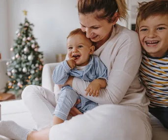 A happy family sitting together with a toddler in pajamas, a Christmas tree in the background.