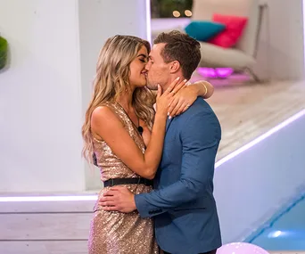 Couple kissing during a romantic moment on Love Island Australia, dressed in elegant attire by the poolside.