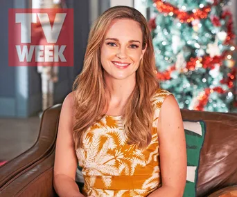 Penny McNamee in a floral dress smiles in front of a Christmas tree, with TV Week logo in the corner.