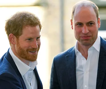 Two men in formal attire smiling, outdoors in daylight.