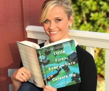 Woman smiling while holding and reading "Little Fires Everywhere" by Celeste Ng outdoors.