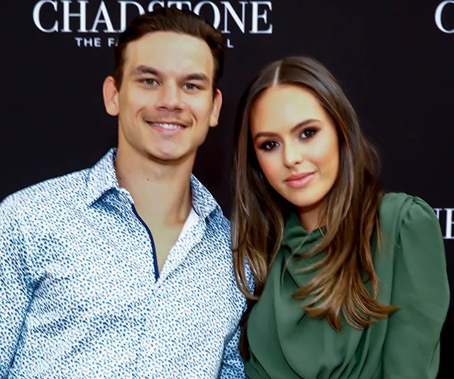 Young couple posing at a Chadstone event, wearing stylish outfits with a black backdrop.