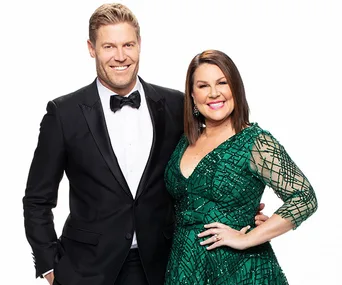 Man in a black tuxedo and woman in a sparkling green dress posing together, both smiling against a white background.