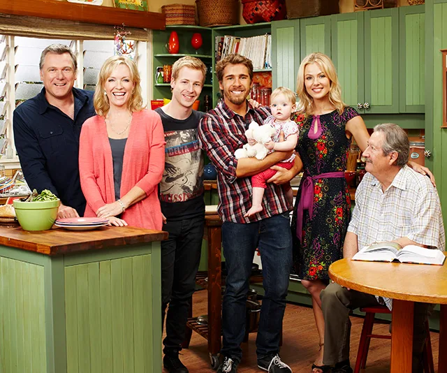 Group photo in a kitchen setting from the TV show "Packed to the Rafters," featuring six adults and a baby.