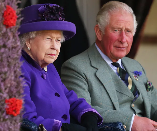 Elderly woman in a purple outfit sitting beside an elderly man in a gray suit at an outdoor event.